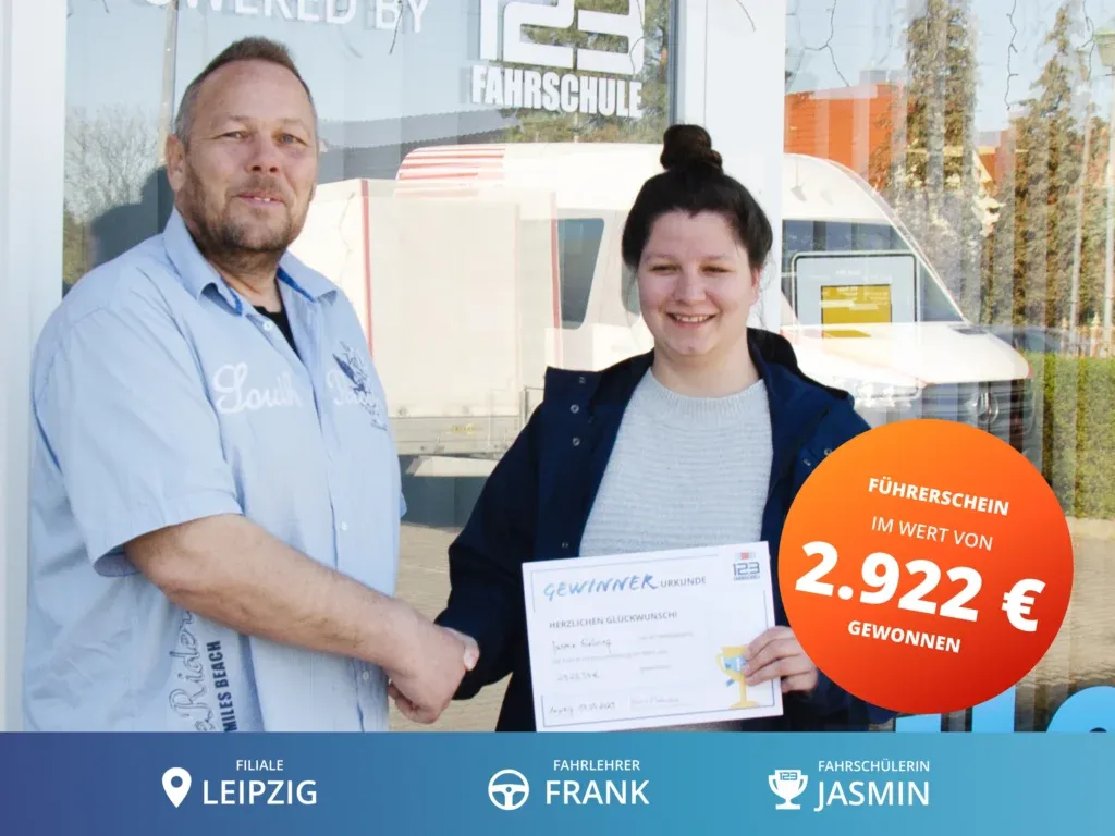 Fahrschülerin steht rechts vom Fahrlehrer und hält eine Gewinnerurkunde im Wert von 2.922€ für die Führerscheinausbildung in der Hand