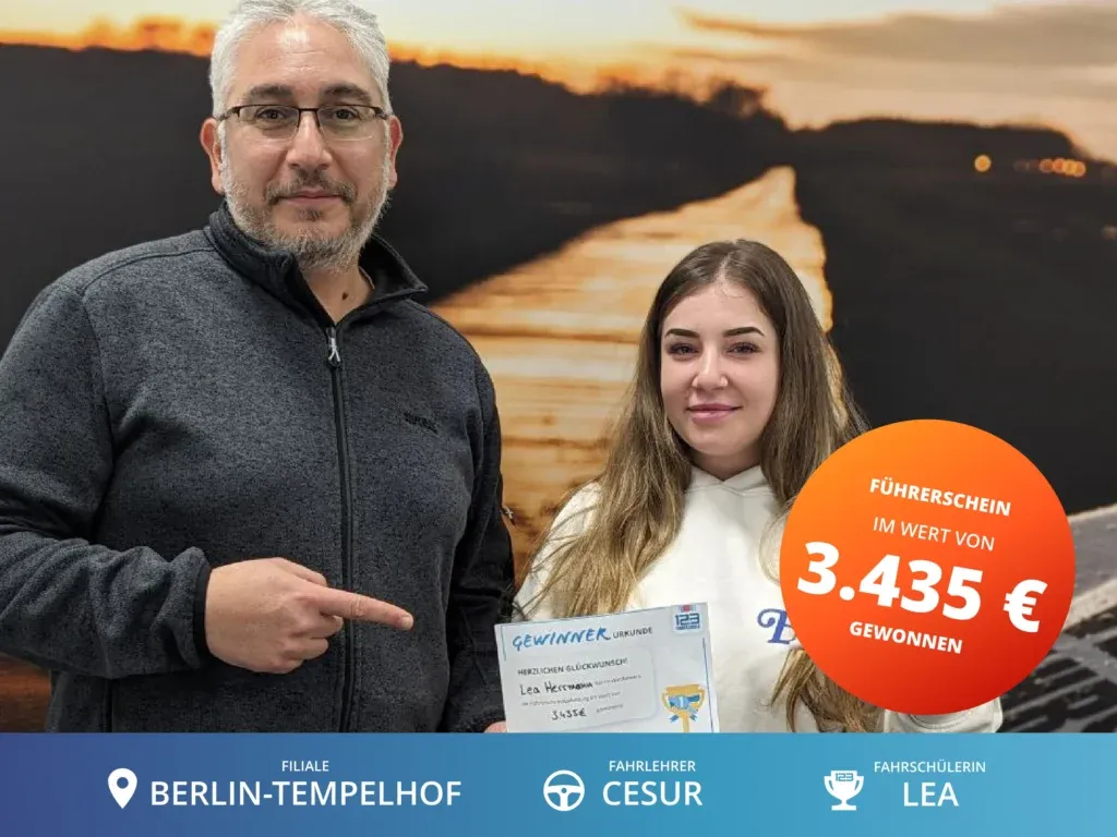 Fahrschülerin steht rechts vom Fahrlehrer und hält eine Gewinnerurkunde im Wert von 3.435€ für die Führerscheinausbildung in der Hand