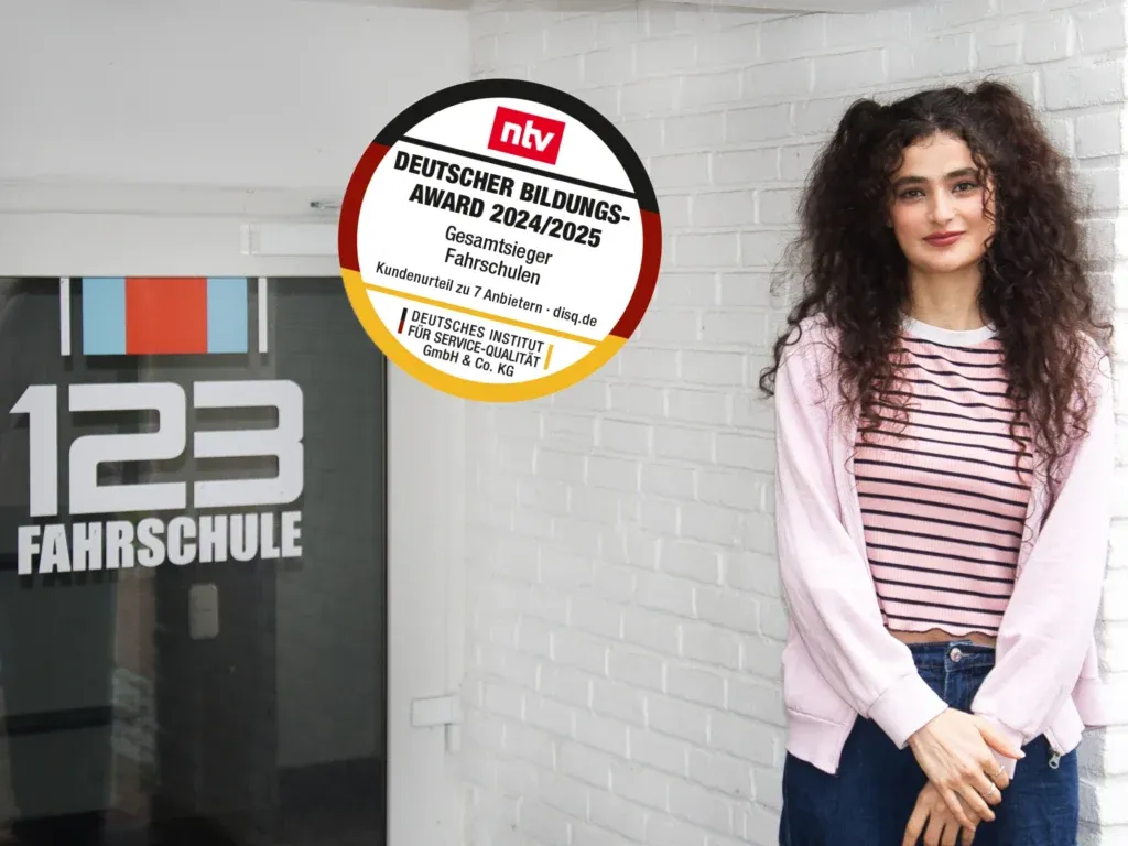 Schülerin der 123fahrschule steht angelehnt an eine weiße Mauer vor dem Gebäude der 123fahrschule.