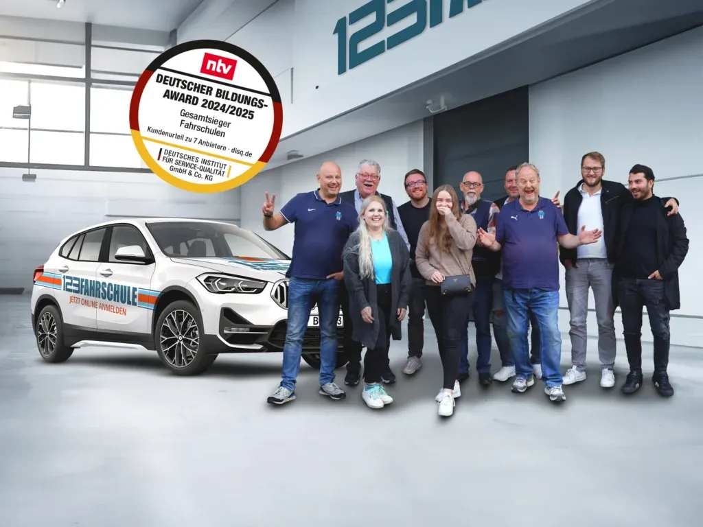 Gruppe von Mitarbeitern der 123fahrschule stehen vor einem Fahrschulauto. Über ihnen befindet sich das "Deutscher Bildungs-Award 2024/2025" Siegel