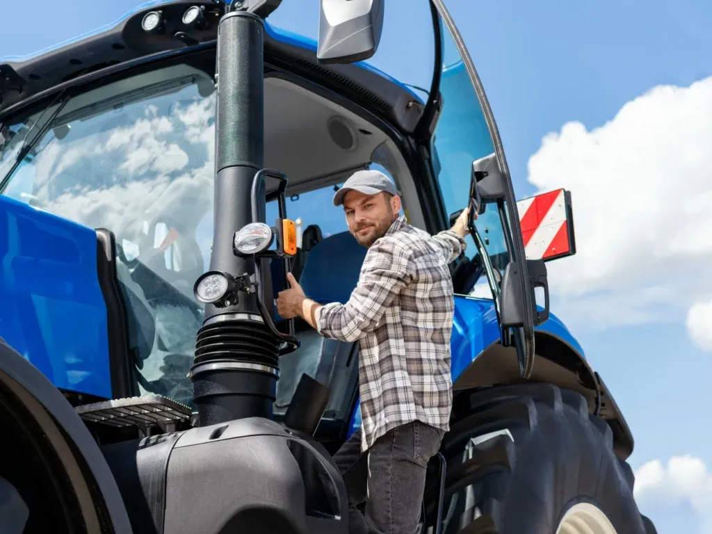 Junger Mann steigt in einen blauen Traktor ein