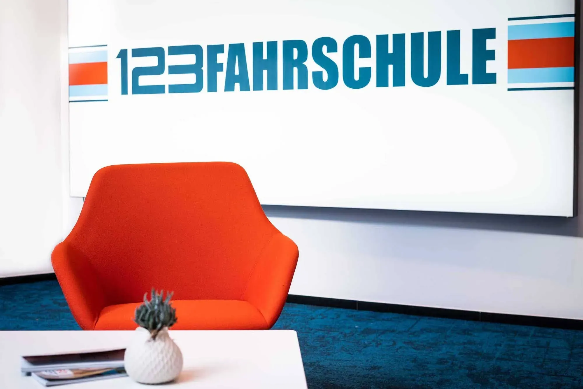 Ein roter Sessel steht vor einem Beistelltisch in einer Fahrschule