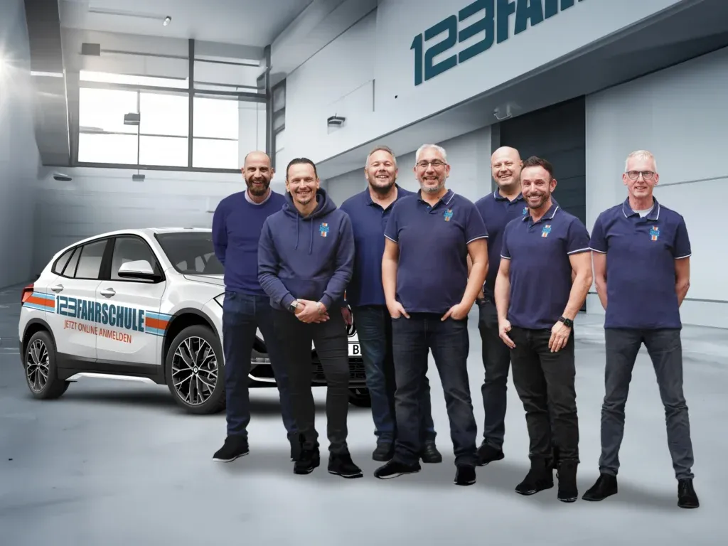Mitarbeiter der 123fahrschule in dunkelblauen Poloshirts mit dem 123Logo stehen vor einem Fahrschulauto