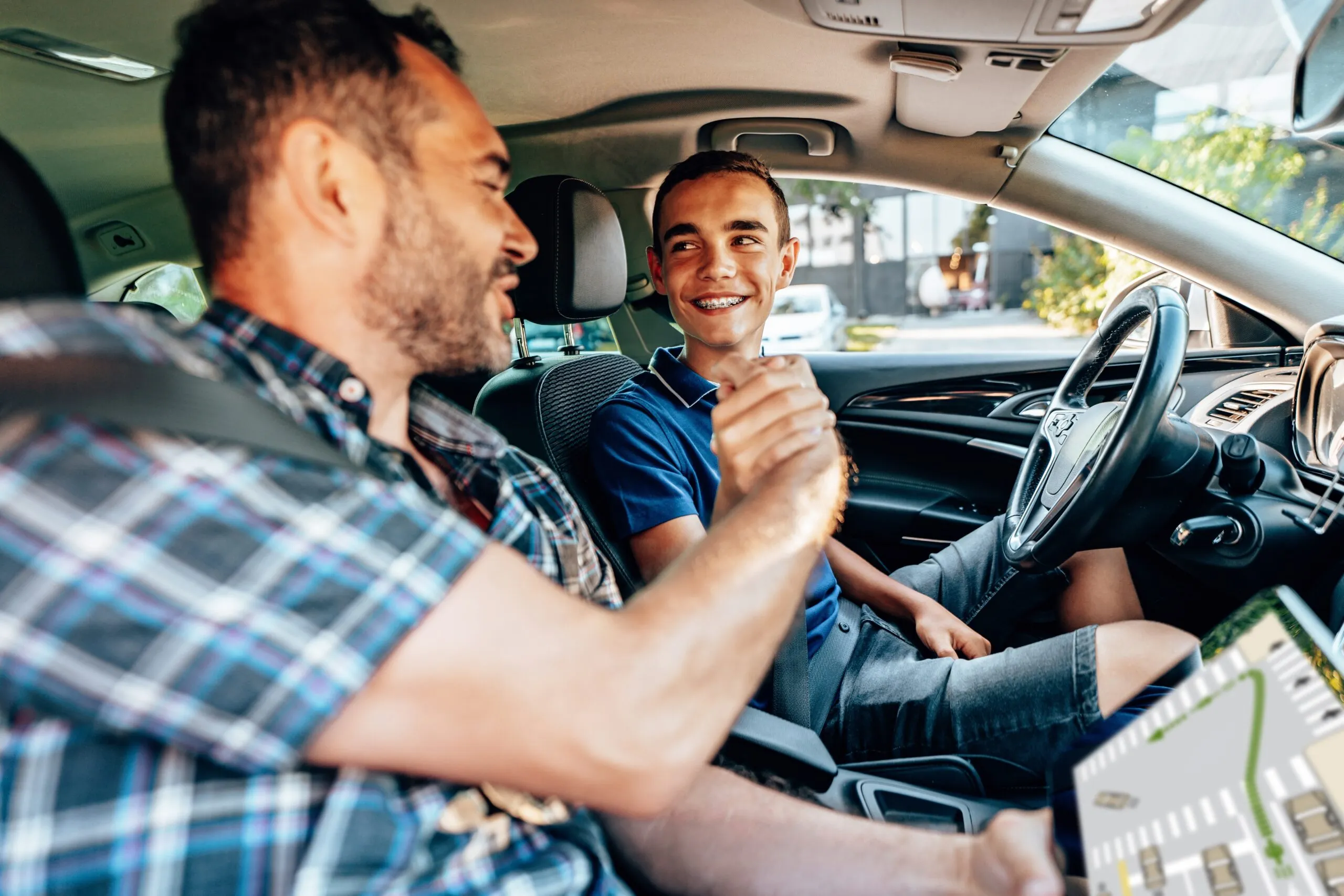 Ein Fahrlehrer gibt seinem Fahrschüler einen Handschlag und dabei lächeln beide.